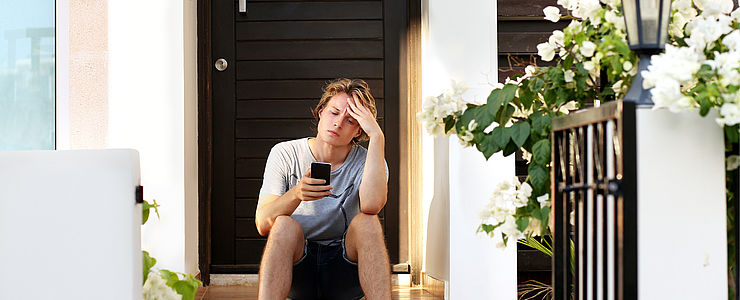 Ein junger Mann hat sich ausgesperrt und sitzt vor der verschlossenen Tür.