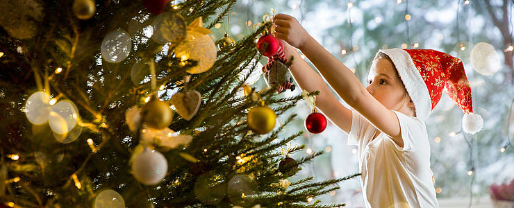 Ein Mädchen schmückt den Christbaum in der Wohnung