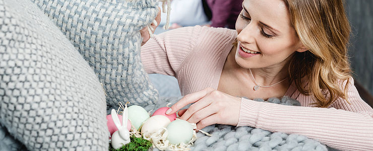 Frau versteckt Ostereier in der Wohnung unter einem Polster.