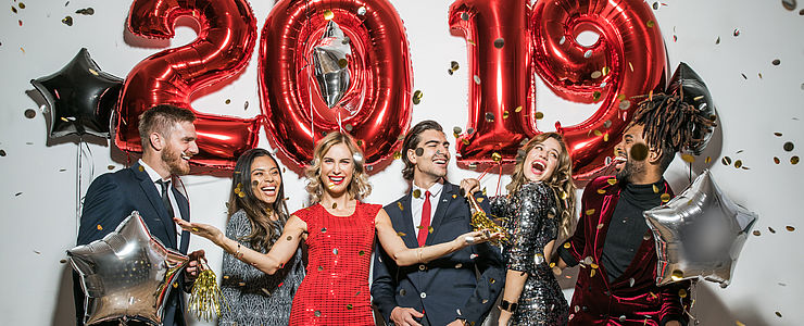 Feiernde Menschen vor einem Schriftzug aus Ballons der das Jahr 2019 formt.
