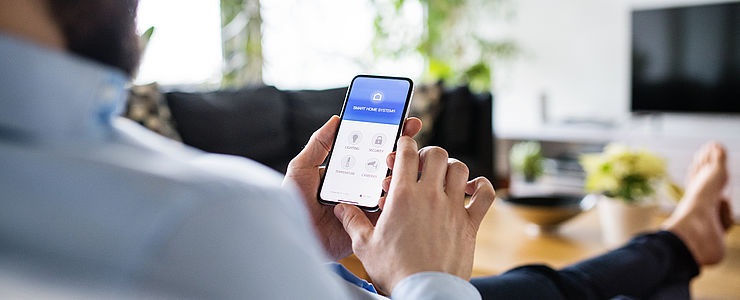 Ein Mann benutzt eine Smart Home App auf seinem Smartphone.